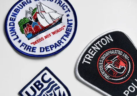 Three embroidered patches: Lundensburg Fire Department with a sailboat, Trenton Police patch with a mermaid, and a UBC patch.