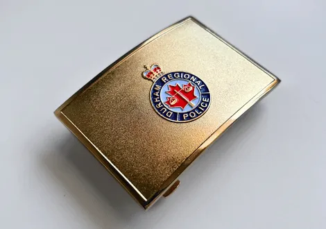 Gold belt buckle with Durham Regional Police emblem featuring a red maple leaf and a crown.