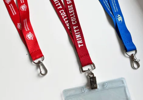 Three branded lanyards in red, maroon, and blue colors with silver clips, one attached to a transparent ID badge holder.