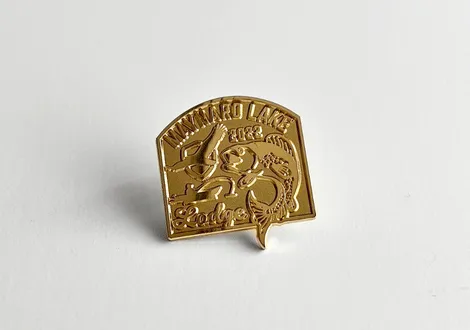 Gold-colored pin with a fish, fishing rod, and the text 'Inawaro Lake Lodge'.