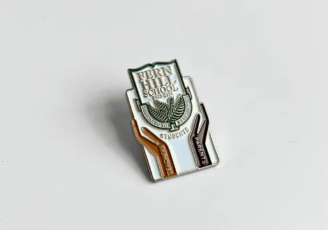 Fern Hill School pin with two hands holding a shield emblem labeled teachers and parents. Example of a custom lapel pin.