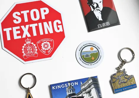 Collection of various keychains and magnets including a red octagonal stop texting sign, a Kingston magnet, a Sand & Sea Burgeo Newfoundland keychain, and a Halifax Beach Provincial Park sticker.