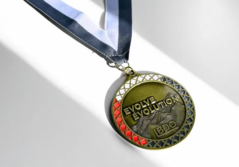 Gold medal with the text 'EVOLVE EVOLUTION BDO' and mountain design on a white surface with a blue and white ribbon.