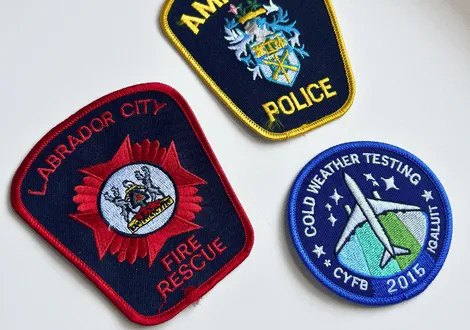 Three embroidered patches: Labrador City Fire Rescue patch, Amarillo Police patch, and Cold Weather Testing CYFB 2015 Qalluit patch with an airplane and stars.