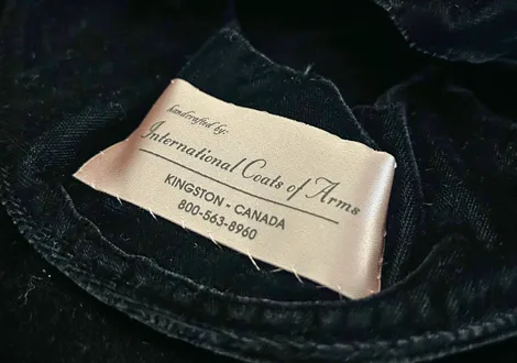 Clothing label for International Coats of Arms with contact information in Kingston, Canada, sewn onto black velvet fabric.